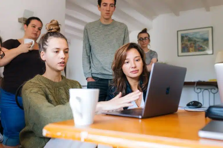 woman in green top using macbook beside group of people